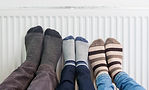 Three peple with their feet against a radiator.
