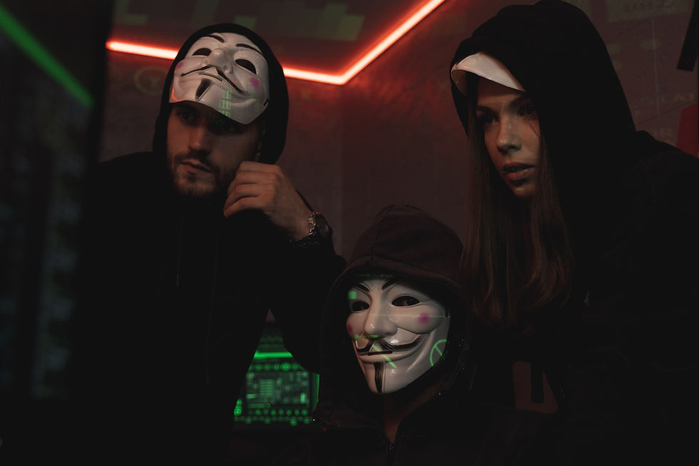 three people wearing masks in a dimly lit room looking at a monitor