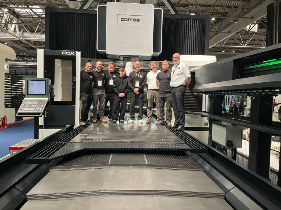Seven people pose on a large CORREA FOX industrial machine in a factory hall, with control panels and metal platforms.