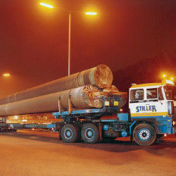 Stiller truck transporting large industrial pipes at night