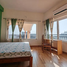 A bright and comfortable retreat room with a bed, wooden desk, and large windows overlooking scenic views during a spiritual and healing retreat with Aarak School and Adhyakula in Rishikesh