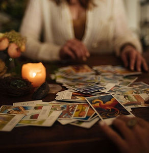 A person reading a spread of tarot cards on a wooden table with a glowing candle, featured in the explore other programs section at Aarak.