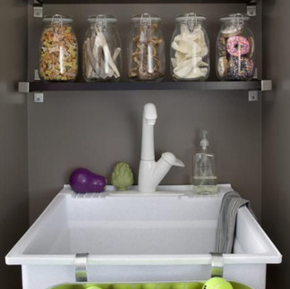A sleek gray shelf holds large glass jars of dog treats and toys. Below, a white tub is filled with bright green tennis balls, with a small sink built into the unit.