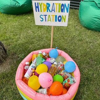Plastic tub filled with colorful water balloons under a “Hydration Station” sign on grass.