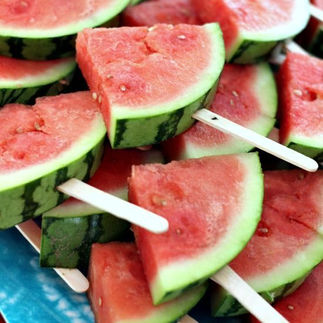 Plate piled with fresh watermelon slices, each served on a wooden popsicle stick for easy grabbing. The slices are arranged on a bright blue platter, creating a fun and refreshing summer treat display.