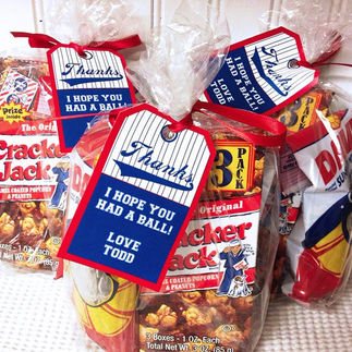 Clear treat bags filled with Cracker Jack snacks and baseball-themed goodies, tied with red ribbons. Each bag has a blue and white tag that reads 'Thanks! I hope you had a ball! Love, Todd,' styled like a vintage baseball ticket. The setup has a fun, sporty theme perfect for party favors or team thank-you gifts.
