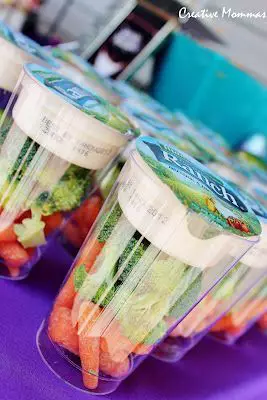 Clear plastic snack containers filled with cut vegetables and fruit lined up on a table.