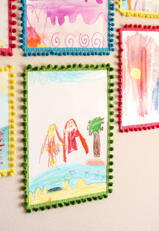 Colorful handmade frame with crayon drawings and decorative borders displayed on a wall, featuring childlike artwork and bright patterns for a DIY gift idea.