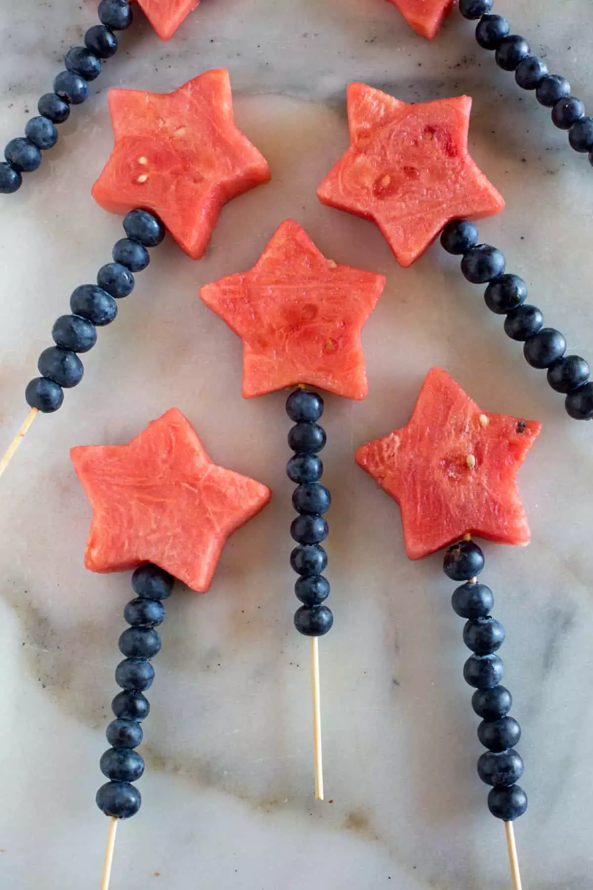 Fruit skewers with star-shaped watermelon and blueberries arranged on sticks.