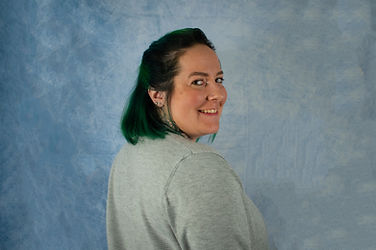 A person with green shoulder length hair smiling and looking over their shoulder at the camera