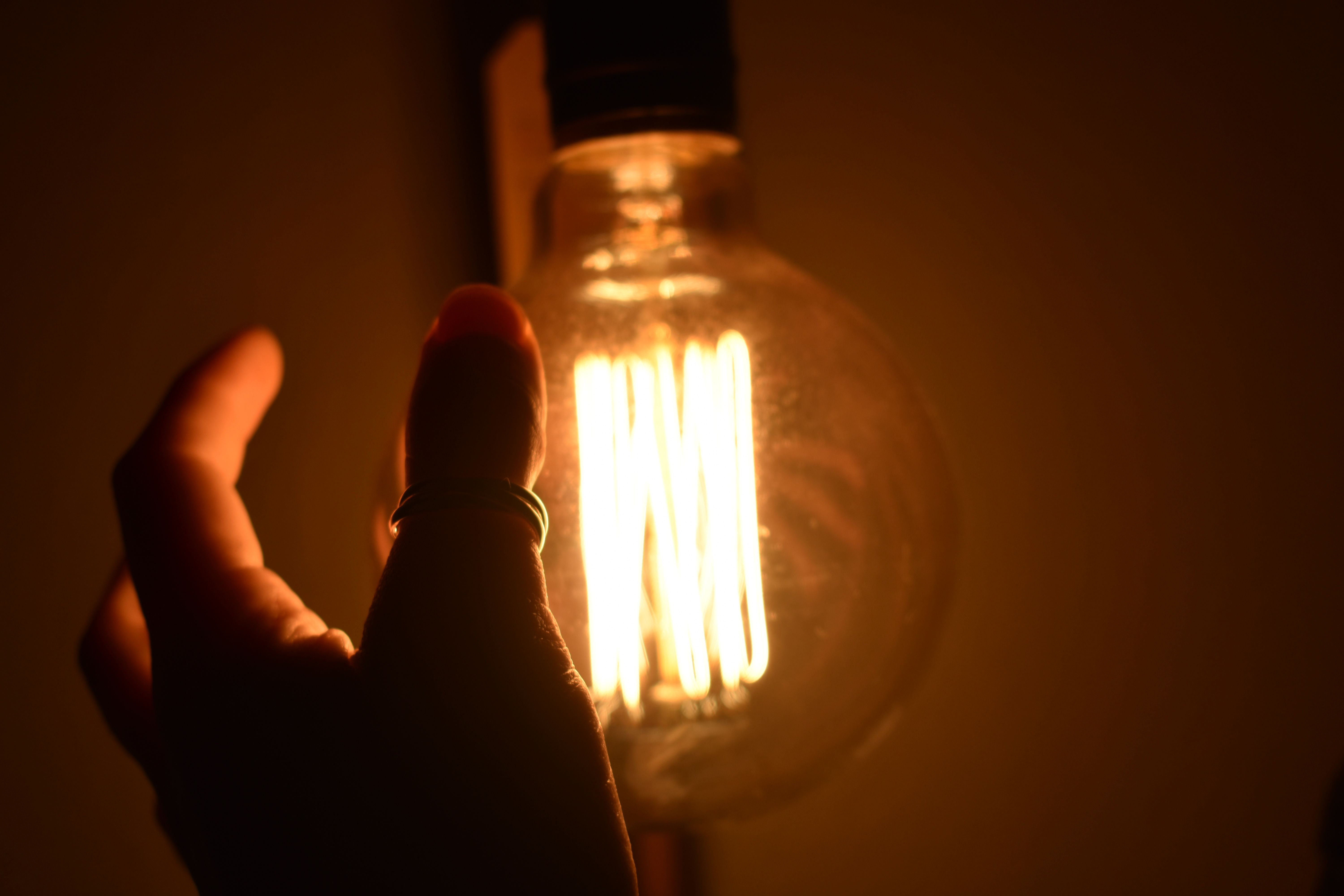 A hand reaching towards a round old fashioned lightbulb