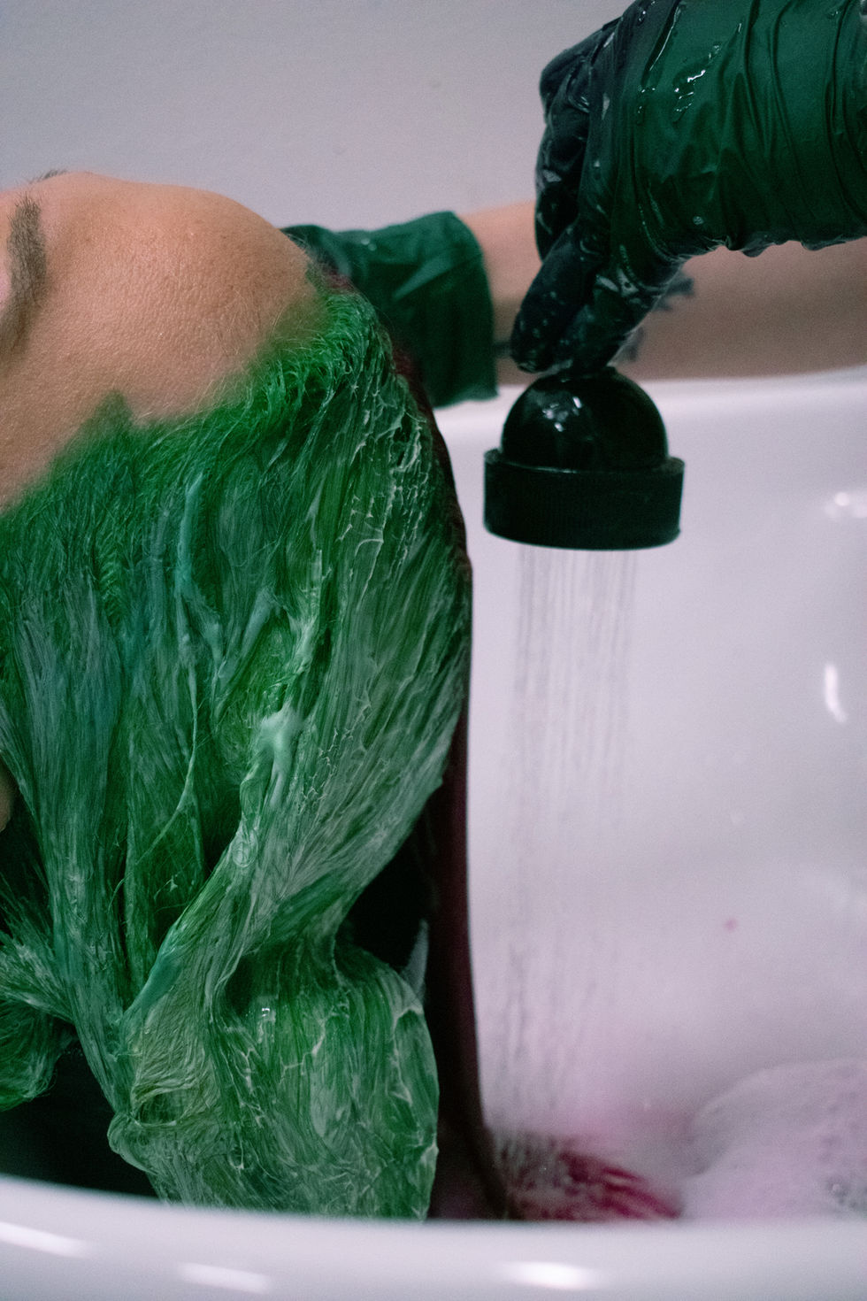 A person with green and pink hair getting it washed by a stylist in the sink