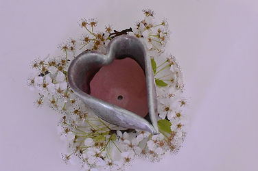 A birds eye view of a heart shaped ceramic pot with flowers around it 
