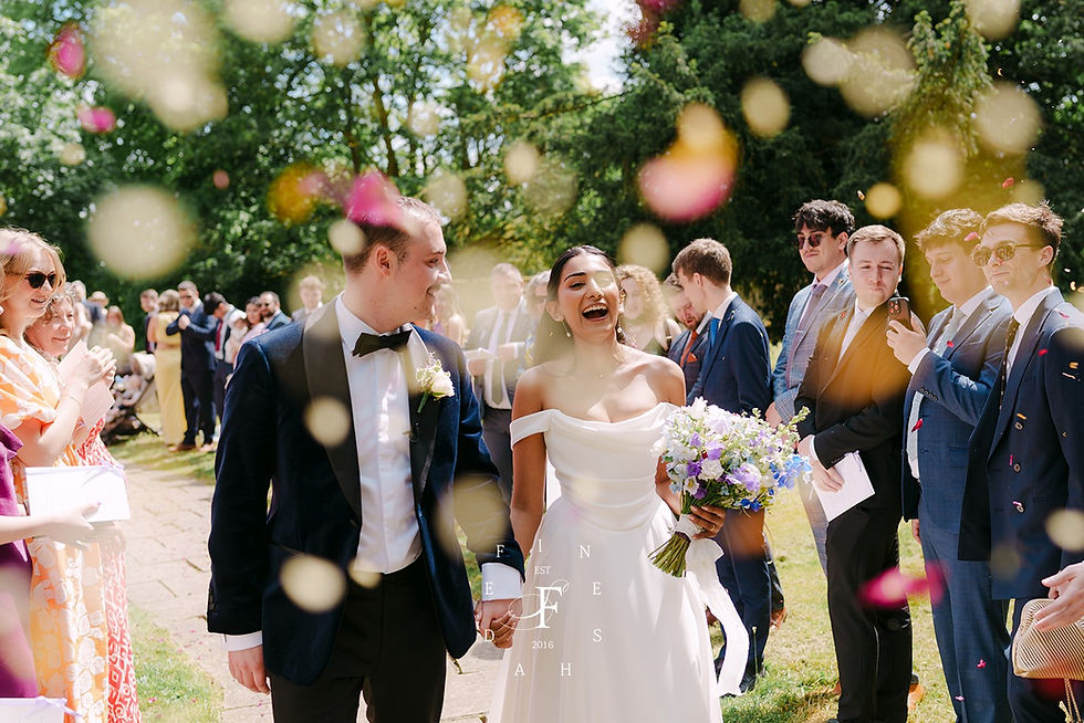A bride and groom walk joyfully through a line of wedding guests throwing confetti.