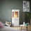 Thumbnail: Lit Rais Nexo 120 Woodburning stove in white with 3 sided glass sat on a glass hearth against a green wall with log basket
