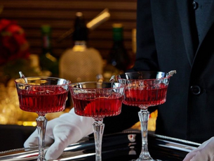 A butler carrying three crystal glasses of G&D — nothing explained, everything implied.