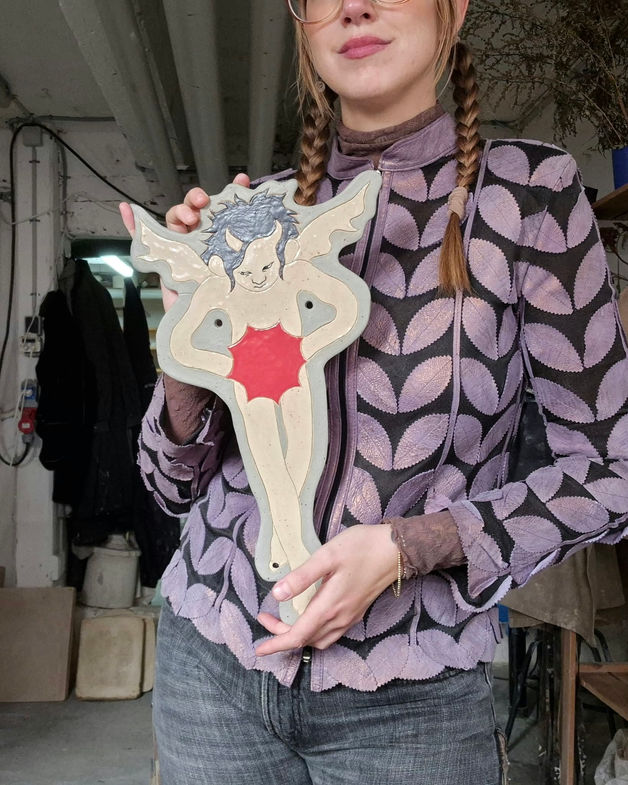 Female ceramicst Christine Lykkeh holding a stoneware wallhanging of a demon