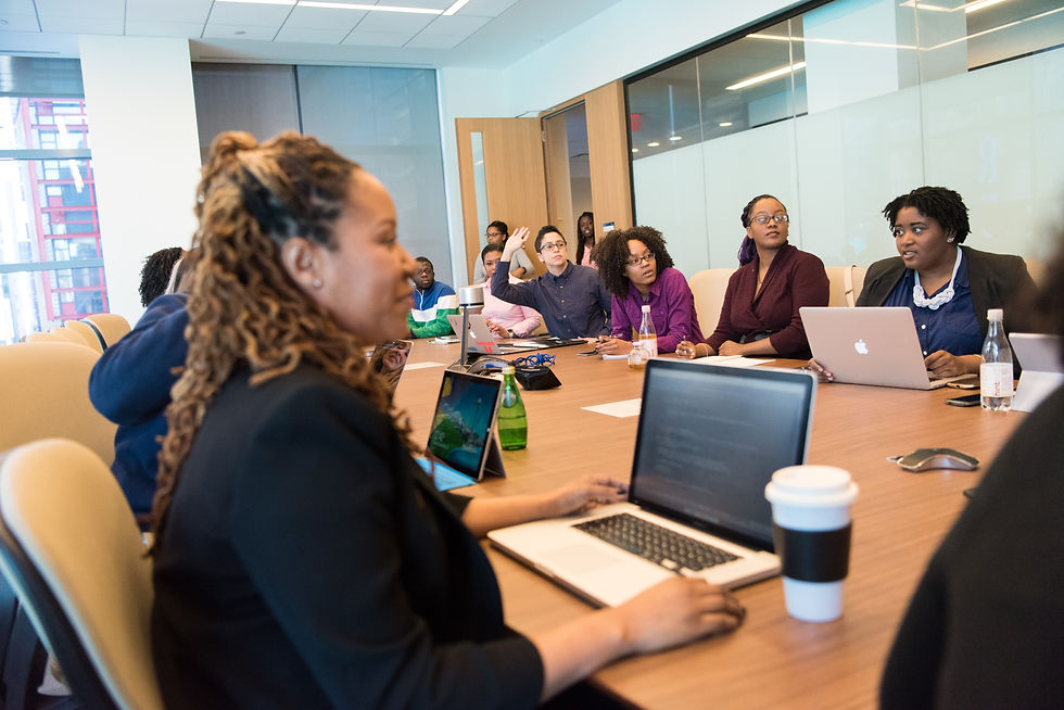women in a meeting sitting around a large desk with laptops and coffee