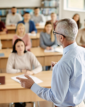 Back view of mature professor giving lecture to large group of college students in the cla