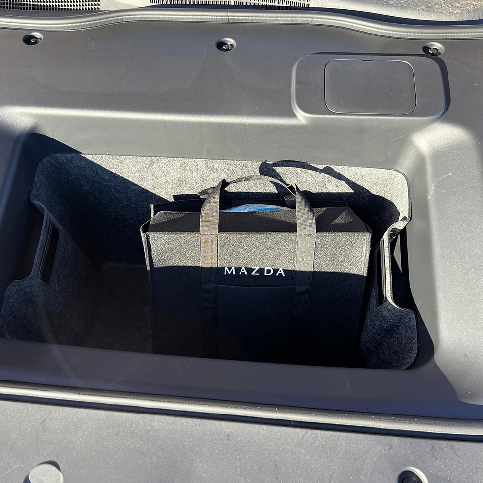 A black Mazda tote bag in a car trunk with gray interior. Sunlight casts shadows on the bag.
