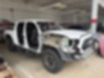 White truck with doors and front fender removed in a garage