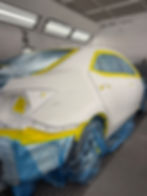 White car masked with yellow tape in a paint booth