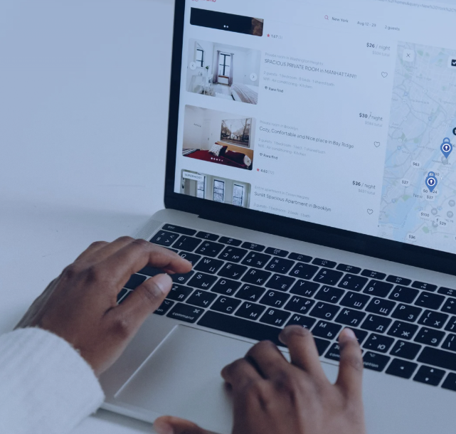 Hands typing on a laptop displaying a booking site with room listings and a map. The mood is focused, with a blue-toned background.
