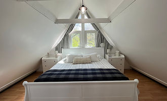 Loft primary suite under the A-frame peak with a king sleigh bed and plaid blanket