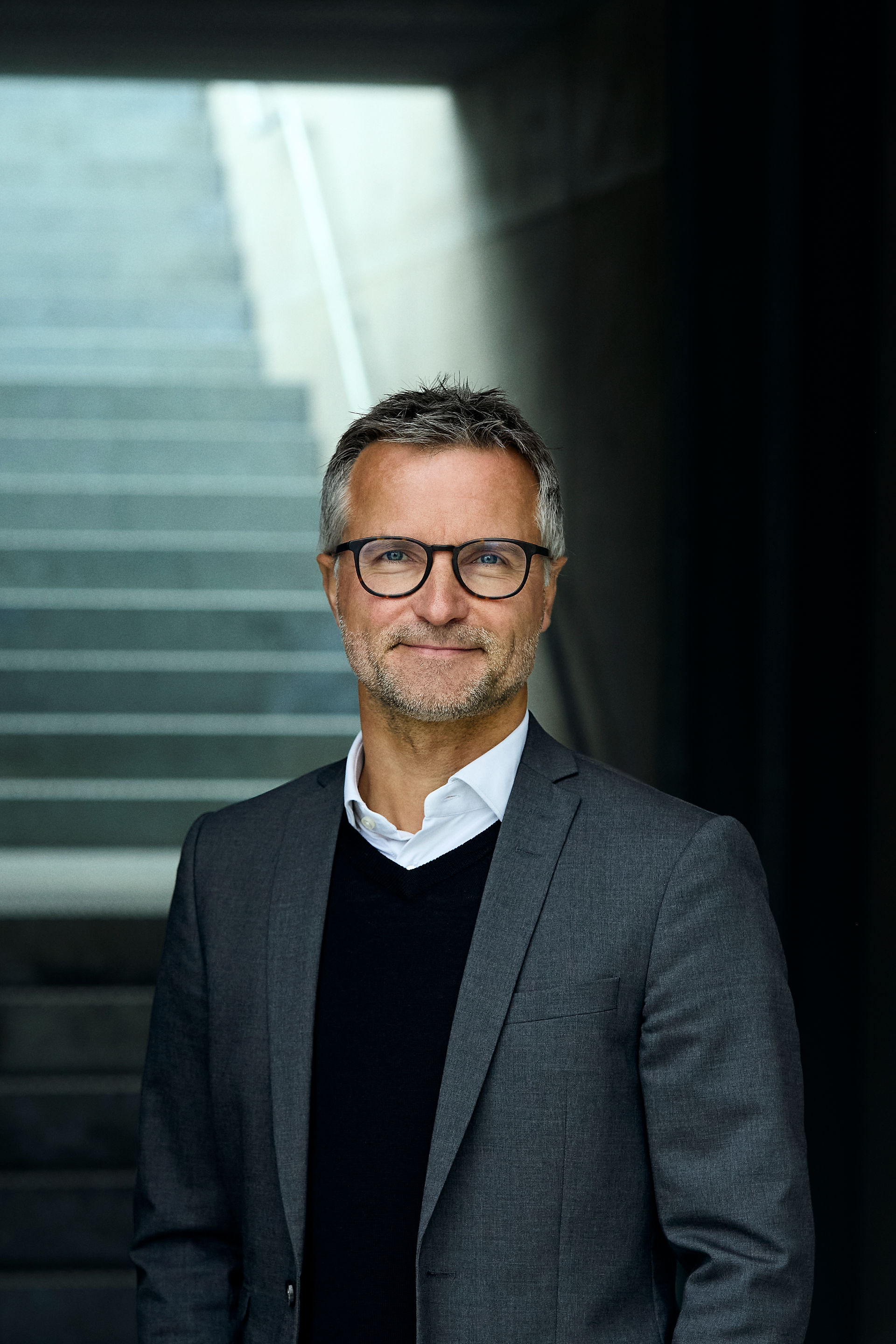 Claus Borum in a dark jumper and business jacket standing standing in front of stairs