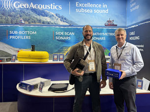 Two men holding sonar equipment on an exhibition stand with a maritime scene as a background
