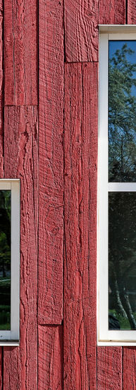 A small window and a bigger window sit side by side on one of the red wood walls. 