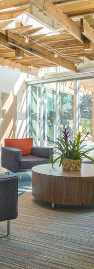 A reading area in the library with chairs and bookshelves. A floor to ceiling glass wall connect the room to an outdoor courtyard. 