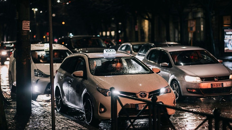 Rainy night street with three taxis and cars lined up, headlights reflecting on wet pavement, moody city traffic.