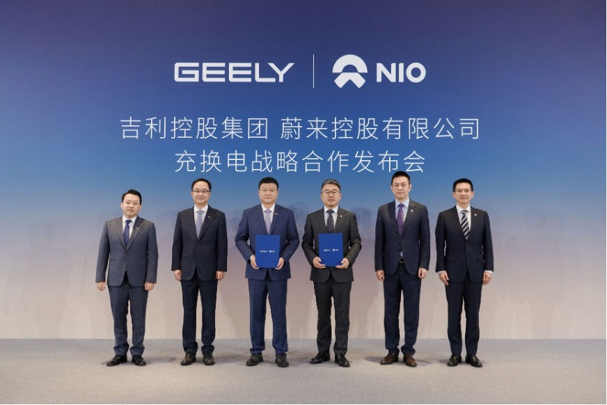 Six suited men stand onstage before GEELY and NIO logos and Chinese event text, holding folders at a partnership launch.