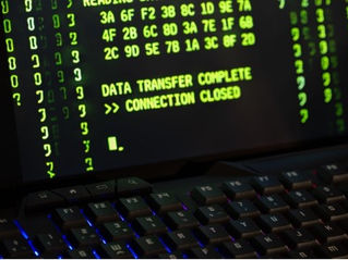Close-up of a laptop keyboard beneath a screen showing green code and the text DATA TRANSFER COMPLETE >> CONNECTION CLOSED.