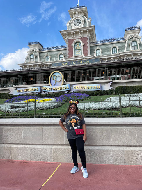 a black woman standing in front of a sign that says the world's most magical celebration for 50 years of Disney world