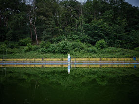 a disguised figure standing at a green swimming pool in the forest.
