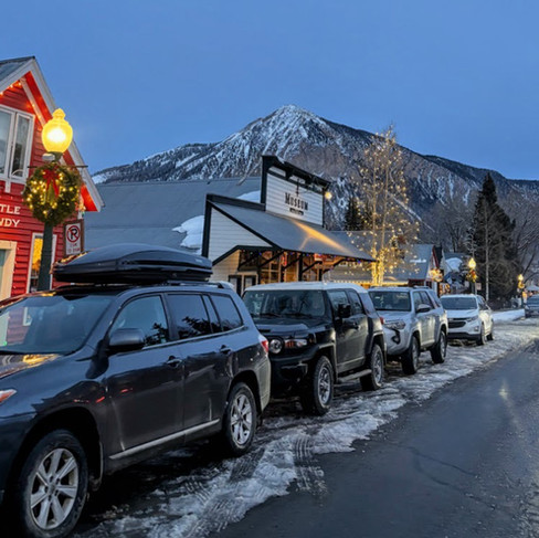 The mountain peak of Crested Butte behind a row of cars and shops on elk avenu