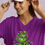 Thumbnail: Smiling woman in white cap, purple t-shirt with mischievous Grinch in curlers.