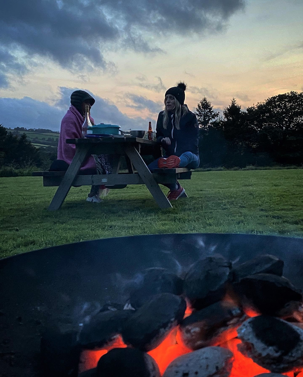 Friends sitting in front of a campfire at Top of the Woods Camping & Glamping, Pembrokeshire Wales.