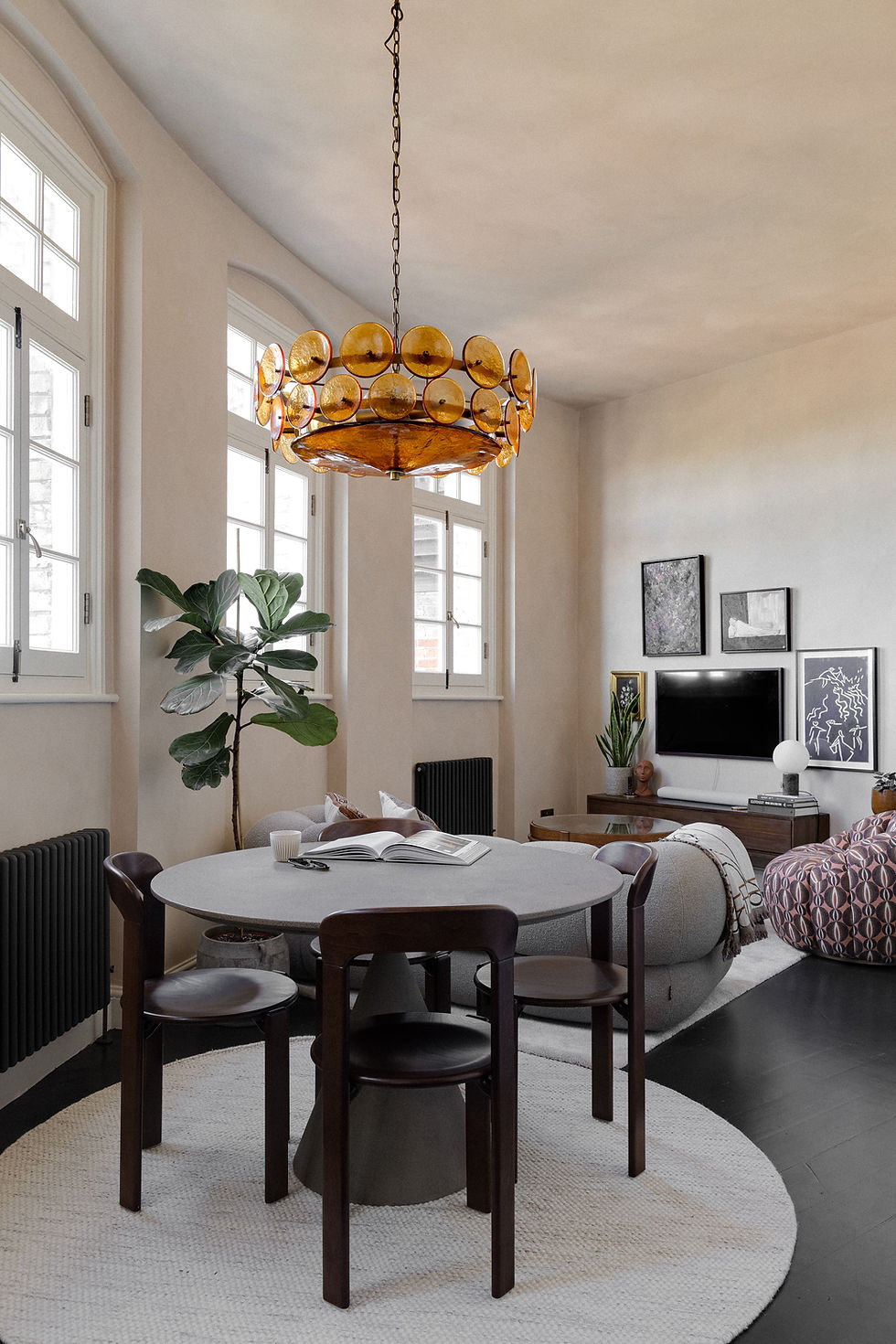 Light-filled living room with creamy limewashed walls, amber Murano glass chandelier, vintage furniture, and layered soft furnishings around a round table.