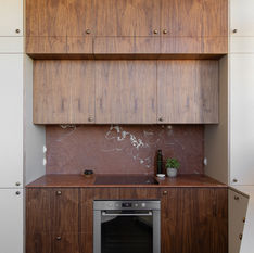 Beautiful wooden kitchen, with neutral colour surrounds, brass hardware for handles for cupboards and a deep red marble worktop and splash back 