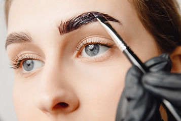 Brow Henna- Blue eyed woman with light brown hair having brow tint being applied to her eyebrow.