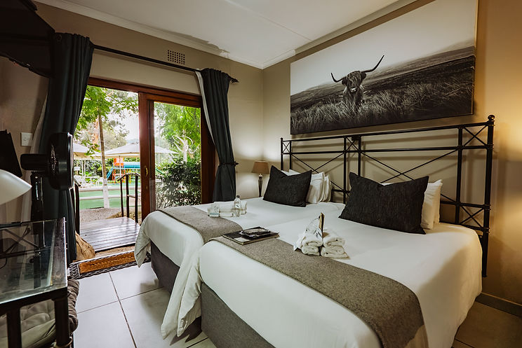 Room with two beds, cow artwork, and open garden door