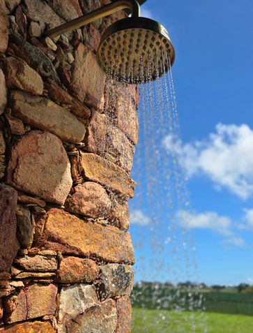 Outdoor shower with water spraying, stone wall, and green field