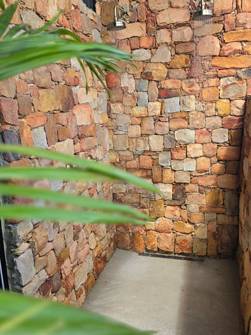 Outdoor shower with stone walls and green foliage