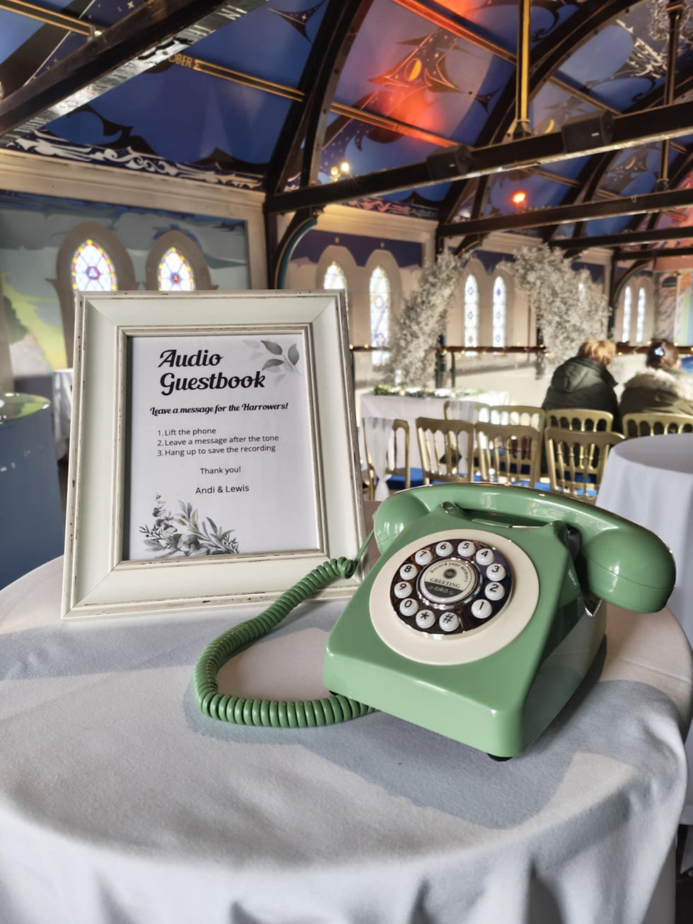 A sage green audio guestbook phone sat on a table next to a cream framed sign in a church.