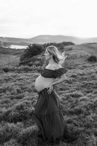 pregnant lady standing in tall grass at sunset