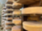 A series of wooden shelves, each filled with wheels of round cheese with reddish rinds (Mountaineer)