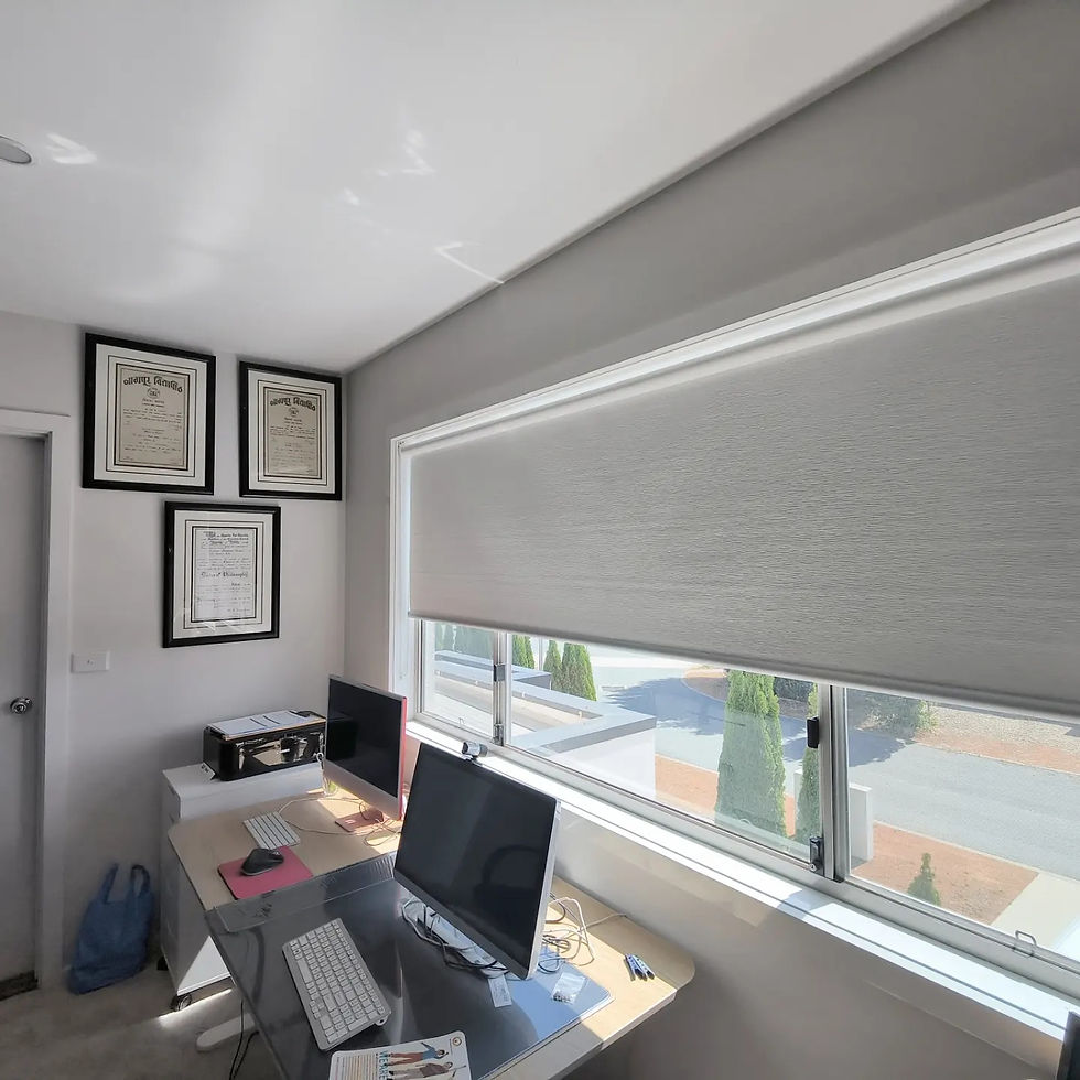 A well-organized home office features sleek roller blinds filtering natural light, complemented by framed certificates on the wall and modern computer equipment on the desk.
